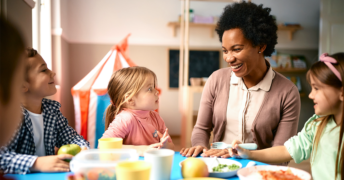 teacher sitting at table during lunch time with group of kids