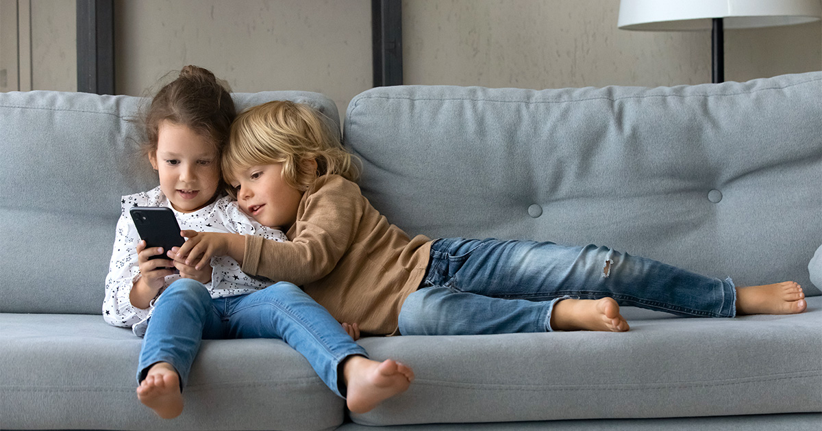Two children sitting on a couch looking at a smartphone together.
