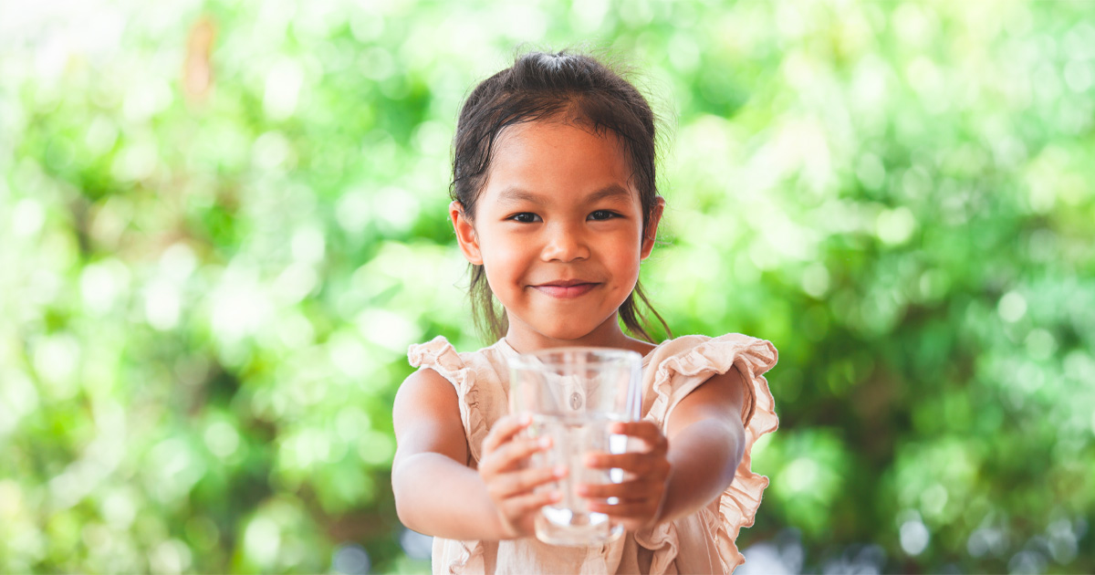A young girl holding a glass of water outdoors.
